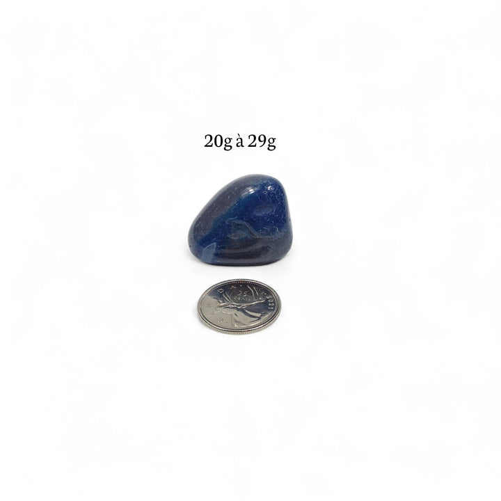 Agate bleue teintée roulée, poids entre 20g et 29g, photographiée avec une pièce de 25 cents pour comparaison visuelle.