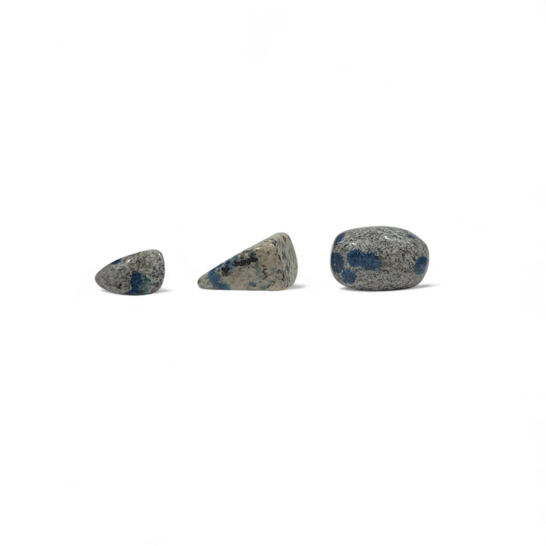 Trois pierres K2 roulées naturelles côte à côte pour comparaison visuelle des tailles, des nuances de gris et des taches bleues d’azurite.