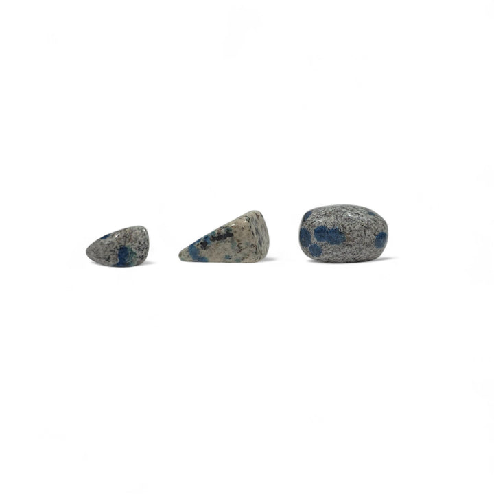 Trois pierres K2 roulées naturelles côte à côte pour comparaison visuelle des tailles, des nuances de gris et des taches bleues d’azurite.